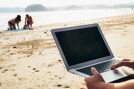 Asian young man with laptop working on the beach. Freedom, remote work, freelancer, technology, internet, travel and vacation conceptsの写真素材