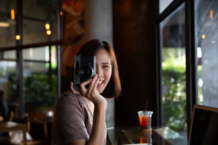 Pretty young hipster woman making photo. Retro photographer. Modern urban girl has fun with vintage photo camera in the cafe or restaurant. City lifestyle concept.の写真素材
