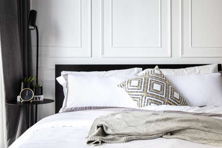 Comfortable bed with soft pillows, bed sheet, knitting blanket. Decorated with matal loft table, clock, small plants and beutiful design of lamp. Bedroom in a modern apartment.の写真素材