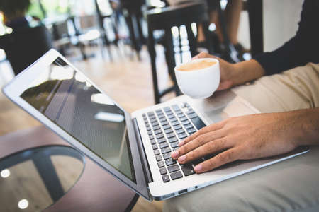 A business man or freelancer working with laptop holding a cup of coffee in cafe.の写真素材