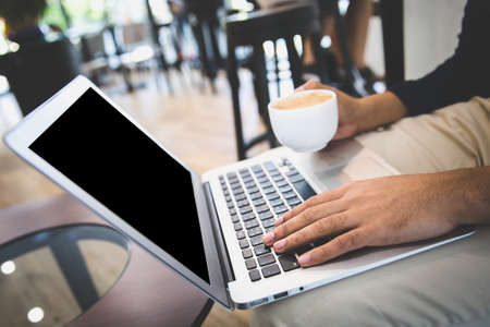 A business man or freelancer working with laptop holding a cup of coffee in cafe.の写真素材