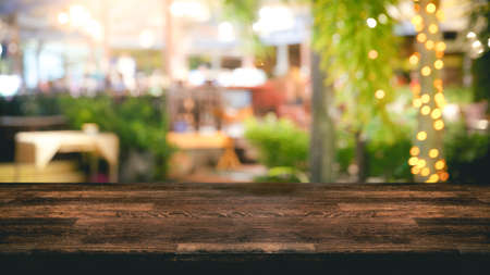 Empty wood table top and Blur light reflection green palm leaves or tree in tropical forest at restaurant, pub or bar at night. Blurred background for product display or montage your products with several concept idea and any occasion.の写真素材