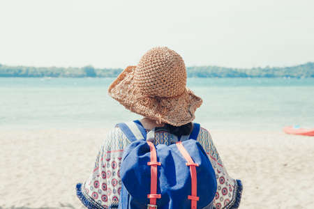 Relax time on summer or holiday concept. Back side view of the Asian girl backpack in straw hat walking and relaxing on the beach and looking forward into the sea. Travelling in Asia.の写真素材