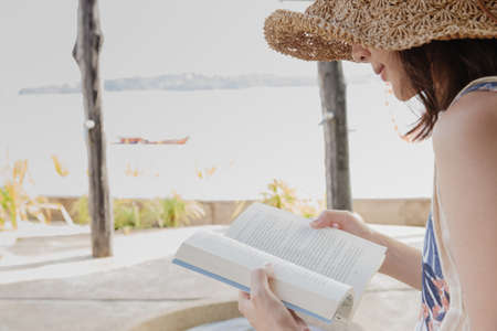 Side view of asian happy woman reading a book on the beach in summer vacation. Relax summer concept. Copy spaceの写真素材