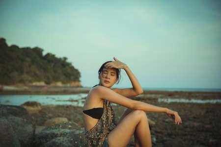 Young woman in casual style fashion Standing on the beach. Relaxing and enjoy holiday at tropical paradise beach. Girl in vacation. Summer vibes. Vintage film grain filter.の写真素材