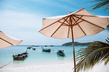 White umbrella on the tropical beach at daytime with long tail taxi boat. People enjoy summer holiday. Vacation concept.の写真素材