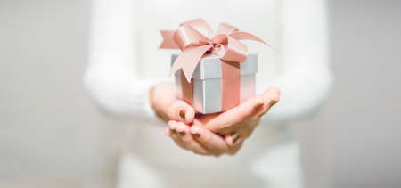Woman hands with white sweater holding a small gift box for special event with copy space....