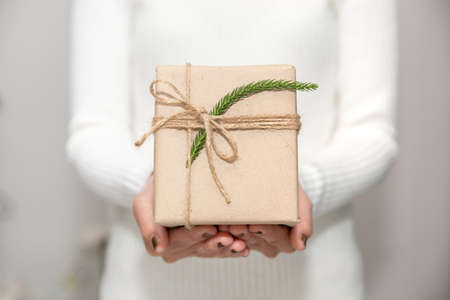 Woman hands with white sweater holding a small gift box for special event with copy space. Christmas, birthday or new year concept.の写真素材