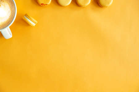 Top view of tasty orange yellow macarons and a cup of coffee. Concepts ideas background on yellow...