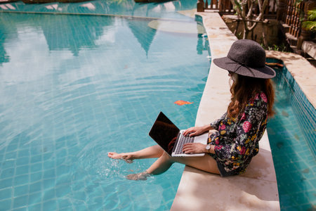 Hipster woman using laptop working as freelancer by the pool in summer time.の写真素材