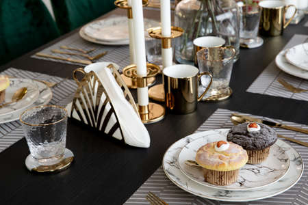 Modern scandinavian living room interior with dining table with mable plates and muffin, design commode, leaf in vase, golden cutlery, and elegant accessories. Template. Stylish home decor.の写真素材