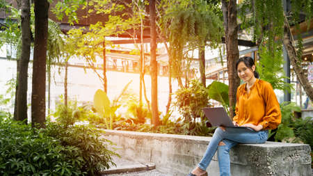 Young woman sitting on ground at forest and working on laptop . Workation concept. Freelancer workの写真素材