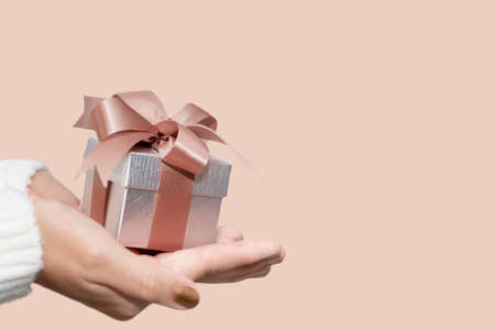 Woman hands with white sweater holding a small gift box for special event with copy space. Christmas, birthday or new year concept.の写真素材