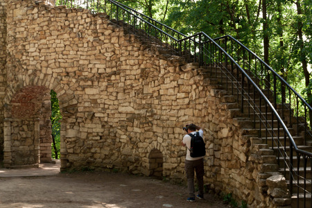 Young man photorgapher at work. Cameraman makes a photo of an ancient wall built in the 18th century from a picturesque yellow stoneの写真素材