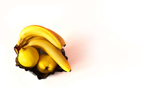 Juicy summer happy yellow banana and quince fruits in a black bowl isolated on white background. A photo with blank free copy space for text.の写真素材