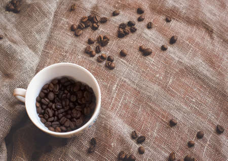 Coffee beans and a white cup on brown rustic raw sackcloth fabric photo. A4 A5 A3 international paper slide poster card with free blank copy space for text.の写真素材