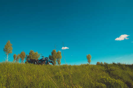 Pleasant summer landscape: old blue sky and clouds, green grass, a sunny meadow and an old retro vintage blue sidecar motorbike. A happy idyllic scenery view and a spirit of travel and adventure.の写真素材
