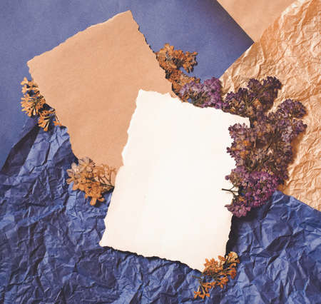 Dry lilac flowers, brown natural craft and white empty sheet on blue, brown crumpled paper flat layout top view. Free blank copy space for text. Design template for card, invitations, wedding decor.の写真素材