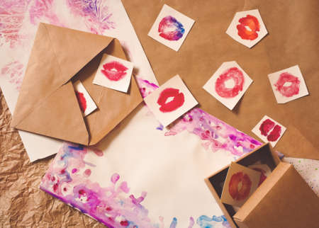 Red lip kiss shapes, brown craft envelope and shipping box flat layout top view on natural and hand-painted watercolor splashes background. Sending love. Template for card, invitation, wedding decor.の写真素材