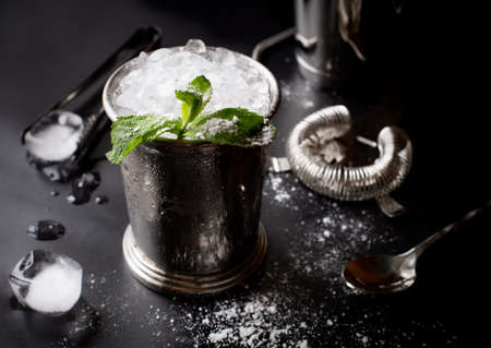 Mint julep whiskey cocktail in misted frozen metal glass and bar accessories shaker jigger spoon ice sugar on black background. Restaurant menu, alcohol recipe decor, specialized website blog design.の写真素材
