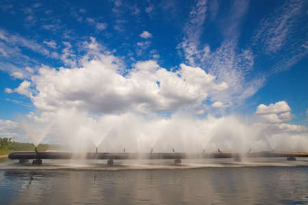 Dukora Belarus Minsk Region. Thermal energy electricity station plant cooling system fountains and lake in sunny summer warm weather. Blue sky and clouds reflecting in the water. Nature and industryの写真素材