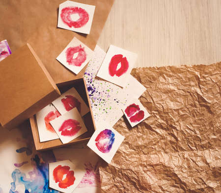 Red lip kiss shapes, brown craft envelope and shipping box flat layout top view on natural and hand-painted watercolor splashes background. Sending love. Template for card, invitation, wedding decorの写真素材