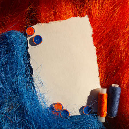 Bright colorful vibrant orange and blue decorative hay, bobbin of thread and buttons around a white...