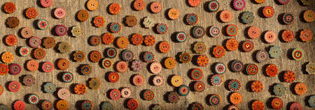 Variety of bright ethnic boho style orange yellow red wooden buttons on brown rustic linen fabric. A...