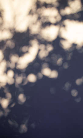 Blue bokeh blurred shadows on a creamy yellow plaster stucco wall in a warm sunny day. An abstract vertical background photo.の写真素材