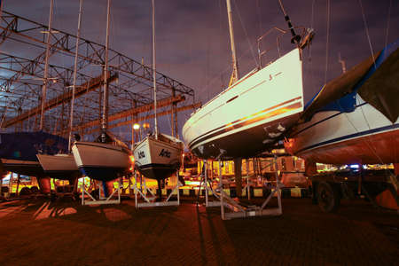 Klaipeda, Lithuania - 11 28 2020: boats at night. Ships and yachts in the winter storage of Baltic port boatyard, beautiful bright colors, purple cloudy sky.のeditorial素材