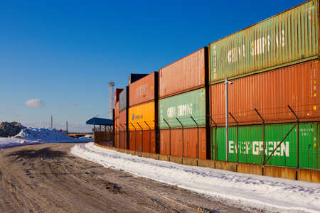Klaipeda, Lithuania - 02 06 21: colored cargo export container in the warehouse of Klaipeda port docks, yellow crane and snowy winter road, deep blue shadows. Sunny colorful photoのeditorial素材