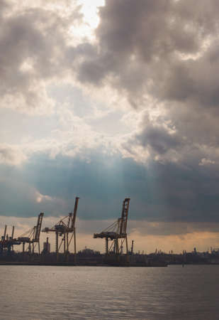 Chornomorsk, Ukraine - 04 20 21: Sea port. Cranes, boats and other industrial constructions, sun light beams, dramatic skyのeditorial素材
