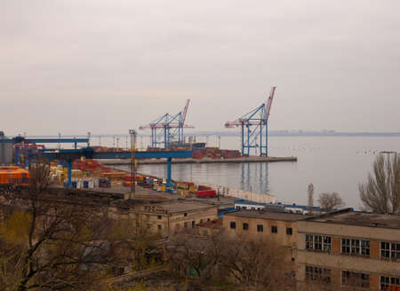 Odessa, Ukraine - 04 19 21: Containers, boats cranes and other industrial constructions in port docks. Gray rainy foggy gloomy weather early spring photoのeditorial素材