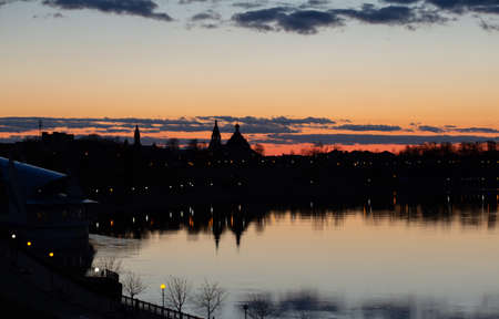 Sunset on Dnieper river. Beautiful Orange cloudy sky, city and church silhouettes reflecting in the river. Pleasant spring photo taken in Rechytsa, Belarus.の写真素材