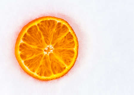 A slice of fresh frozen orange tangerine mandarin fruit on white cold winter snow. A flat lay top view photo with free empty copy space for text.の写真素材