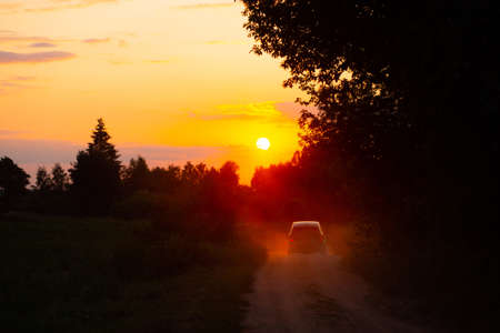 Summer sunset and a lonely car on a dusty road. Warm colors high contrast photo.の写真素材