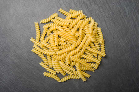 Spiral pasta on a black stone background. View from above. Horizontal photo.