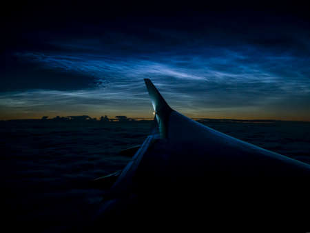 Silhouette of the left wing at cruising altitude above the clouds at night, against the backdrop of...
