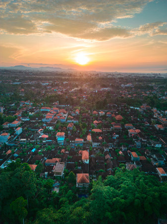 Breathtaking Balinese sunset over green hills and colorful rooftops in Ubud during summerの写真素材