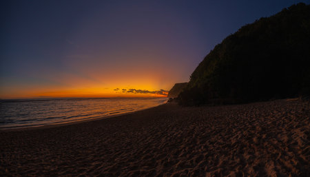 Sunset on Melasti Beach, Bali. Golden light over ocean waves and tropical coastline.の写真素材