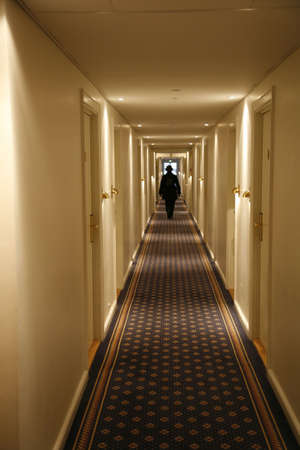 Black dressed person walking down a long hotel corridor. Motion blur.の写真素材