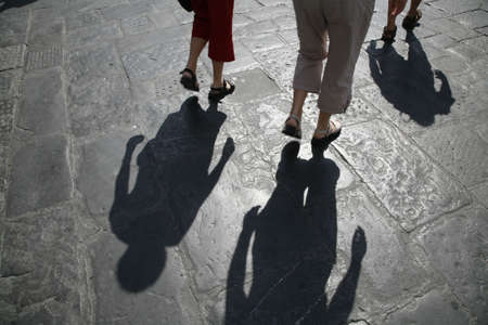 Legs and shadows of tourists in the Italian town Florence. The sun i shining in the worn 1000 years old paving.の写真素材