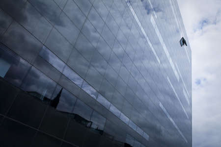 Concept photo. Hope in the middle of the finance crisis. Symbolized by the open window on top of the corporate building. Although the clouds and light are still threatening.の写真素材
