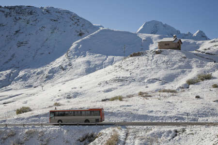 Chapel in the Dolomites in the Veneto province of Northern Italy in late September. Seen from the mountain pass Pordoi 2245 m above sea an early morning after snowfall. A public bus passing by.の写真素材