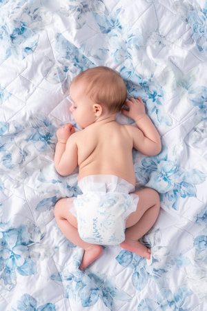 top view of adorable baby in diaper lying on bed with blue flowersの素材