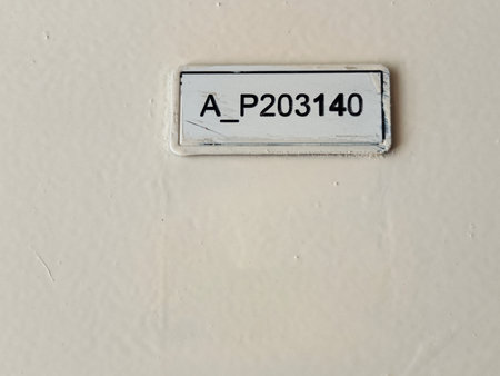 Close up of rectangular wall sign with black printed code A_P203140 on white background.