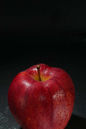 Red wet apple with drops on wet black background. Concept of freshness. Empty space for textの写真素材