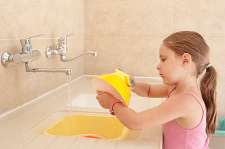 Little caucasian girl (elementary age) washing a dishes outdoor in the camping sink. Summer, camping, active recreation, touristic and education concept.の写真素材