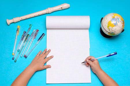 Open notebook with flute, globe, autumn leaves and hands of Caucasian primary school age girl....