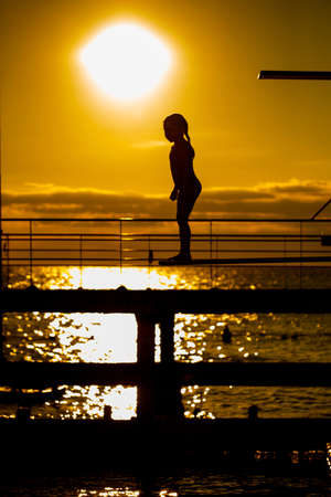 Indecision little girl silhouette on the 3m springboard.の写真素材